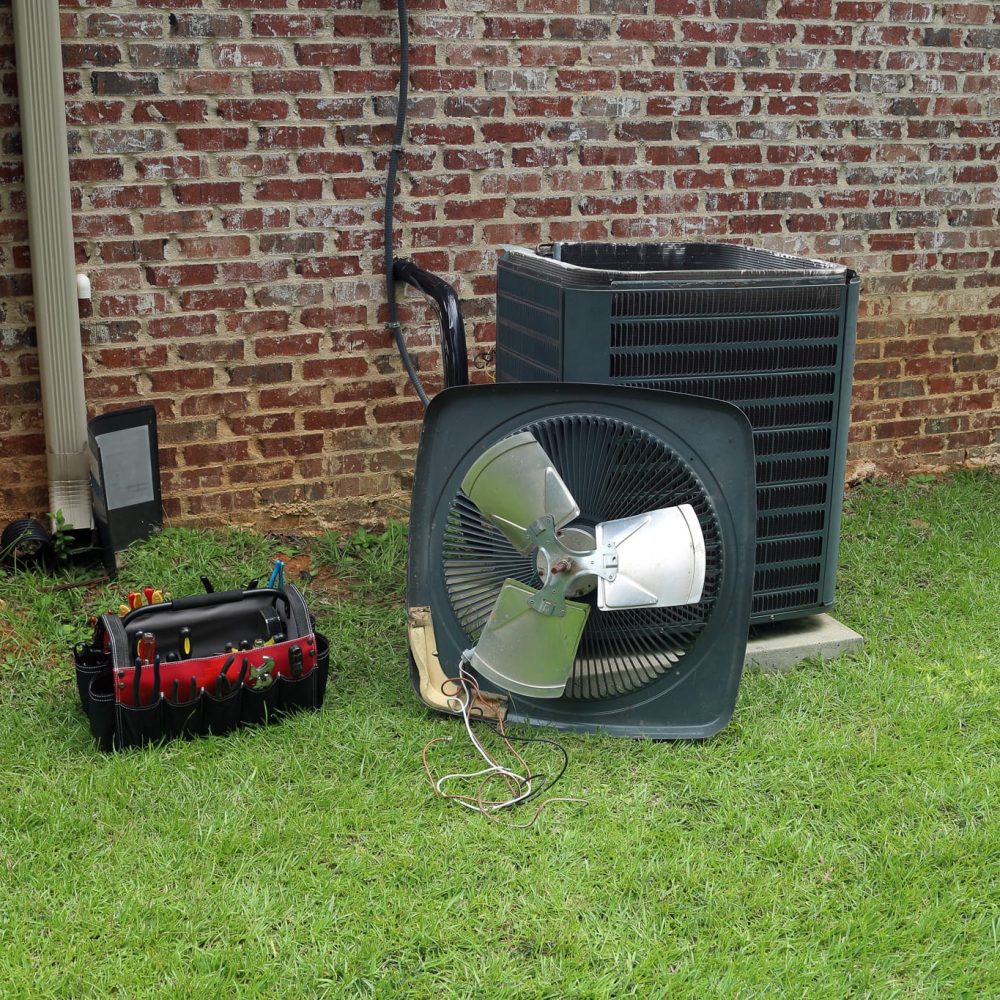 Air Conitioner Condenser coil with tools being repaired Air Conditioner compressor condenser coil with fan and tools being worked on next to a brick house for repair maintenance.